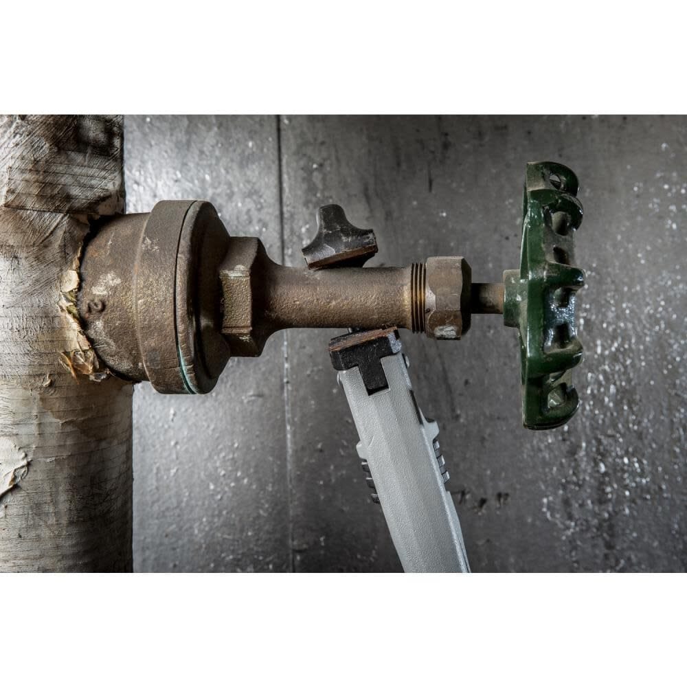 Horizontal view of the Crescent CAPW18 aluminum pipe wrench fitting into a narrow gap to grip a corroded metal joint in an industrial plumbing setup.