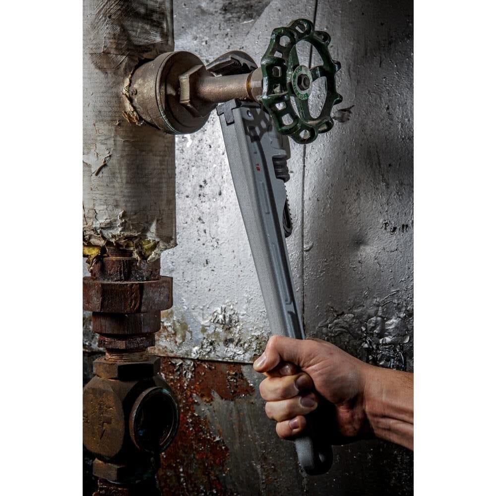 Vertical perspective of a technician using the Crescent CAPW18 pipe wrench to adjust a valve handle on a complex industrial piping system.