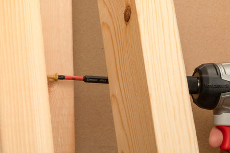 Crescent VORTEX Torx T25 6 inch impact power bit shown in a real-world building application as an operator drives a gold structural wood screw deeply between dimensional framing studs with a high torque cordless impact driver, illustrating its slim reach profile capacity inside deep carpentry pockets.