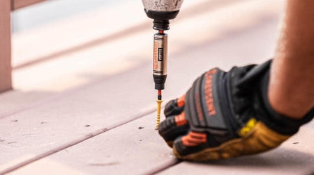 A construction worker wearing safety gloves uses an impact driver equipped with the Crescent VORTEX magnetic bit holder and dual torsion zone extension to drive a long screw into a wooden deck board