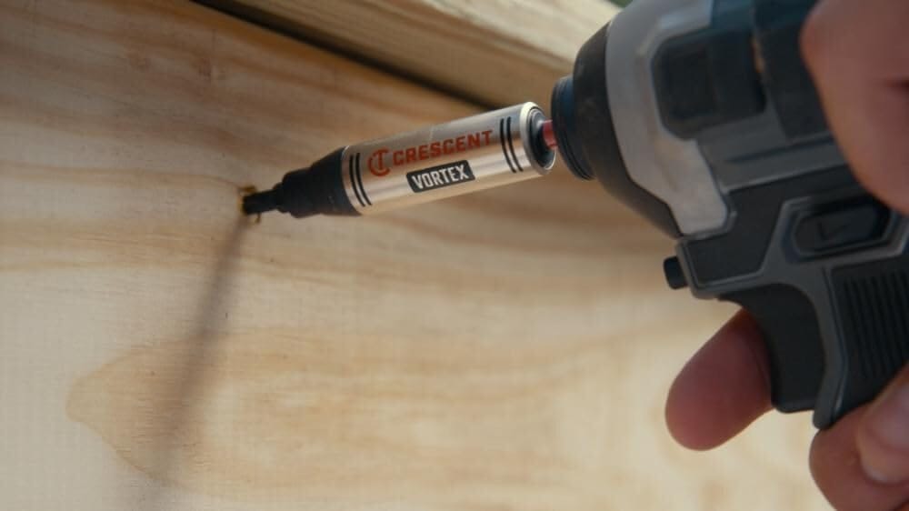 Close-up action shot of a power impact driver utilizing the Crescent VORTEX S2 steel bit holder to effortlessly drive a fastener horizontally into light-colored structural wood framing
