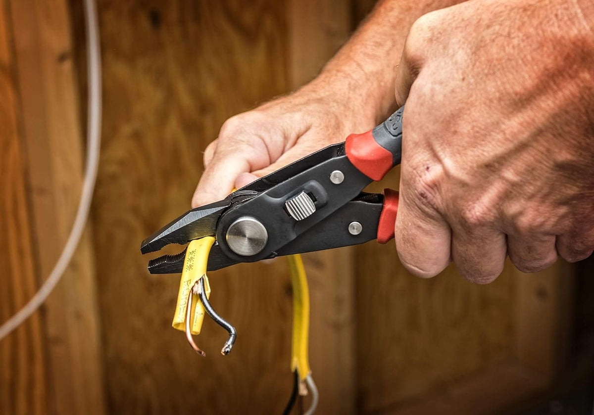 A professional technician using the Crescent CCP8V 2-in-1 pliers to cut through a thick yellow electrical cable, showcasing the tool's heavy-duty lineman's plier functionality.
