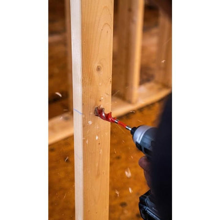 Action shot of a cordless impact driver using a Crescent auger bit to drill through a wooden stud with chips flying.
