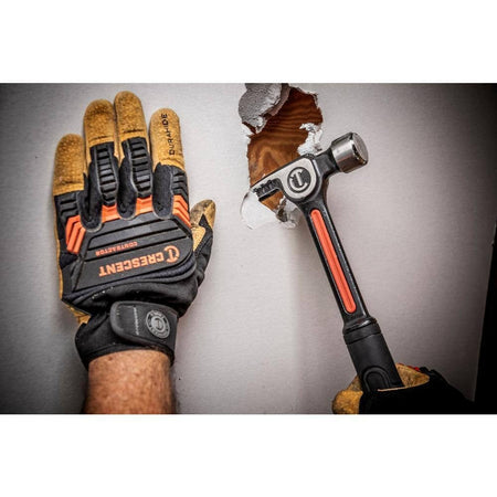 A lifestyle action shot of a tradesperson wearing professional work gloves using the Crescent ripping claw hammer to perform demolition work on a drywall surface, showcasing the tool's versatility and impact force.