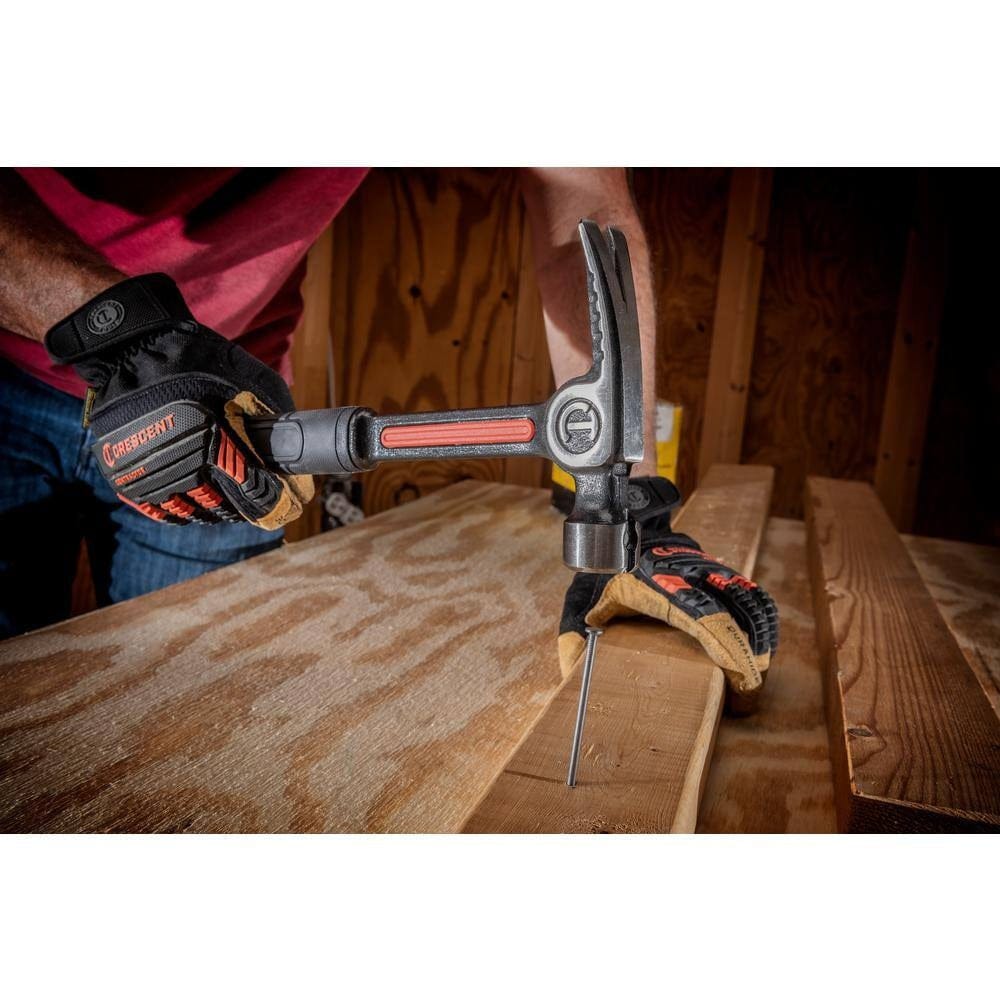 An action photograph showing a professional using the Crescent 20 oz steel hammer to drive a nail into a wooden beam, illustrating the precision balance and reduced vibration of the Vibeguard technology.