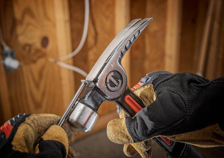 An action photograph of a professional woodworker using the magnetic nail starter on the Crescent 20 oz hammer to set a nail into a wooden stud, demonstrating efficient one-handed jobsite operation.