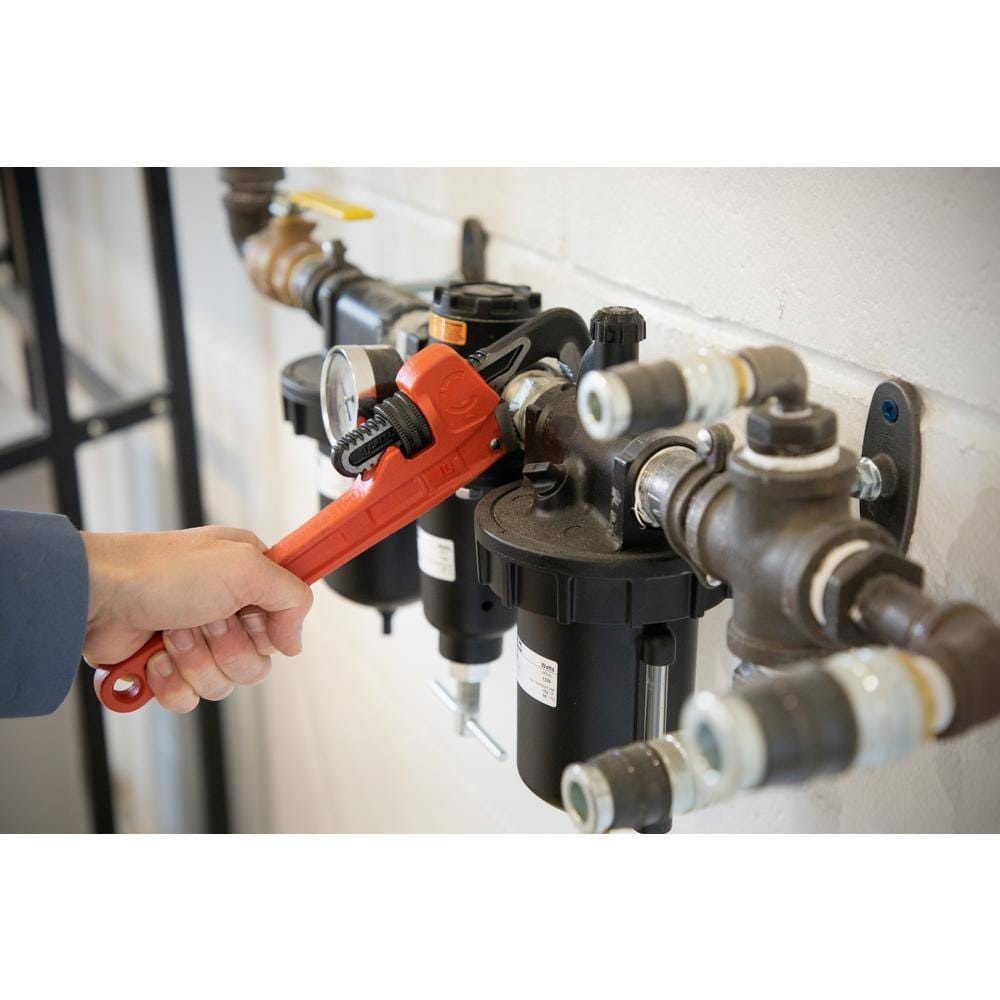 Action shot showing a plumber using the Crescent 10-inch cast iron pipe wrench to adjust a fitting on a residential water filtration system, demonstrating the tool's compact reach.