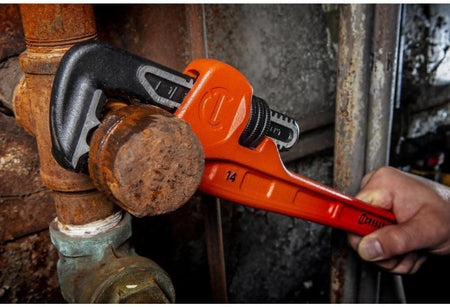 Close-up action shot of the Crescent 14-inch cast iron pipe wrench being used to loosen a large, rusted iron pipe cap in an industrial maintenance environment.
