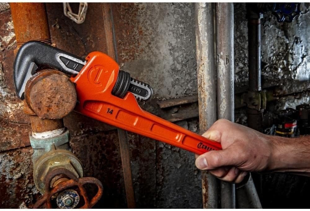 Side action view of a worker using the Crescent CIPW14 wrench to grip a corroded metal pipe, demonstrating the tool's high torque capability and ergonomic handle design.