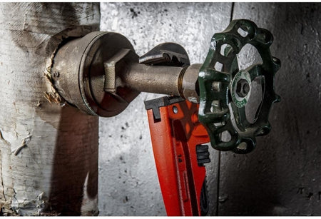 Detailed action shot showing the K9 jaw of the Crescent pipe wrench biting into a brass valve stem at a 30-degree angle for superior access in confined spaces.