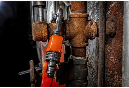 Close-up action shot showing the wrench clamped securely onto a heavily rusted iron pipe fitting, highlighting the grip of the jaw teeth on corroded surfaces.