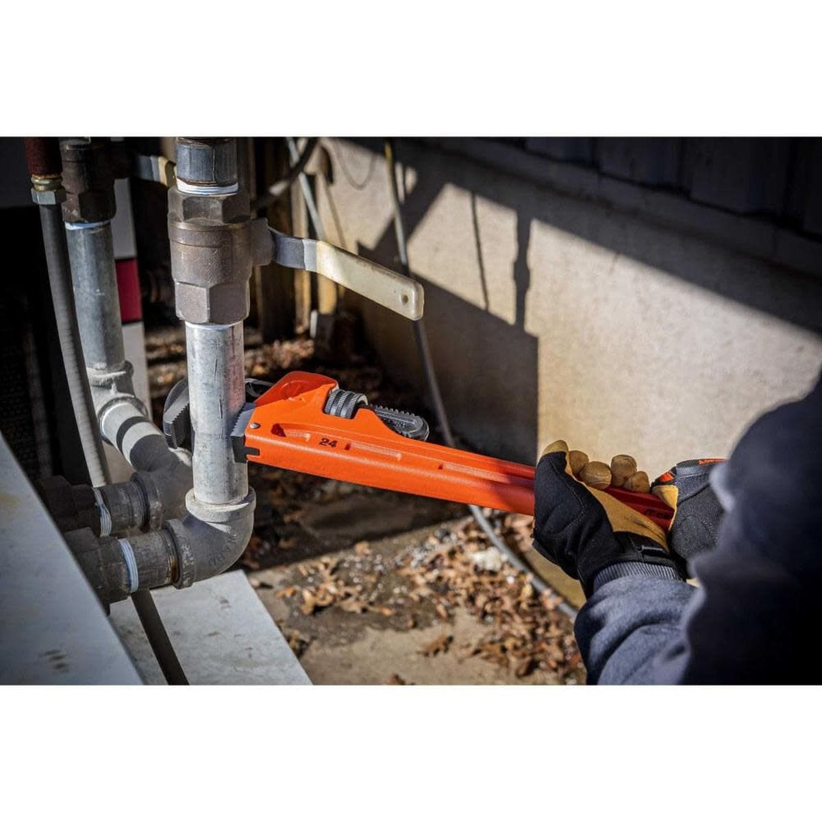 A full jobsite application photo showing the hands of a tradesperson utilizing the red Crescent straight cast iron wrench to securely tighten an exterior structural steel utility pipe array.