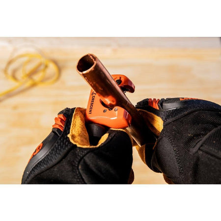 An action photograph of a professional using the Crescent CMPC118 pipe cutter to slice through a copper pipe, demonstrating the tool's compact design and precision performance in residential or commercial plumbing applications.