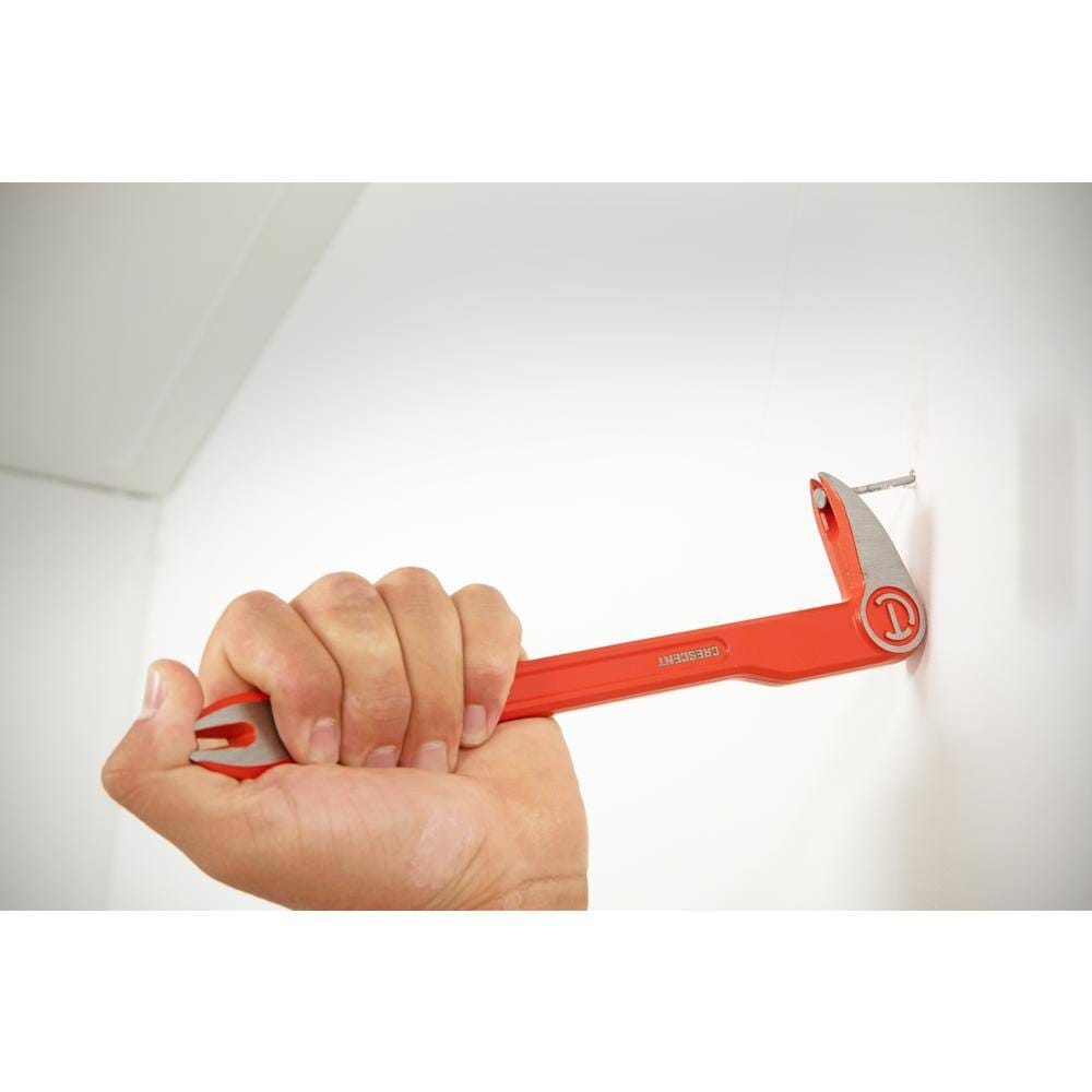 A hand firmly gripping the Crescent 12-inch double end nail puller, using the straight precision ground edge to smoothly pry a nail out of a wall during a wrecking project.