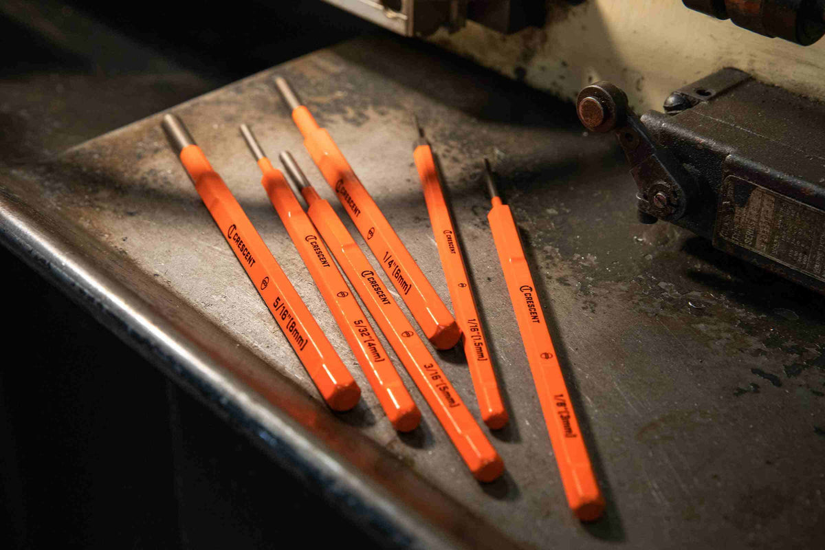 A lifestyle shot of the complete Crescent CPPS456 pin punch set resting on a metal workbench in a professional shop environment, showcasing the high-visibility finish and industrial durability.