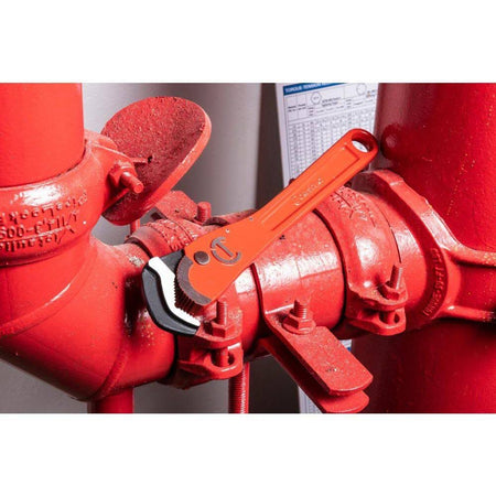 Detailed action shot of the 16-inch wrench jaw locked onto a red industrial pipe fitting, showing how the extended lower jaw provides a superior grip on large diameter workpieces.