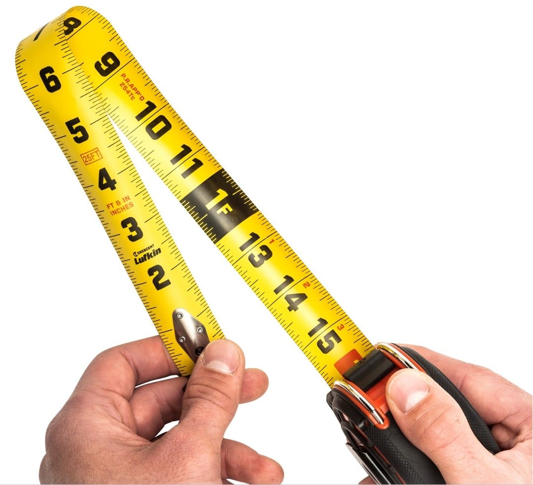 Close-up demonstrating the dual-sided blade of the Crescent Shockforce tape measure, showing standard SAE measurements on the top and vertical quick-read markings on the underside for overhead use.