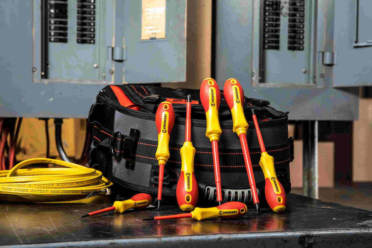 Crescent CTVDESDS electrical hand tools arranged around a canvas tool bag in a workshop setting with an open electrical breaker box in the background.