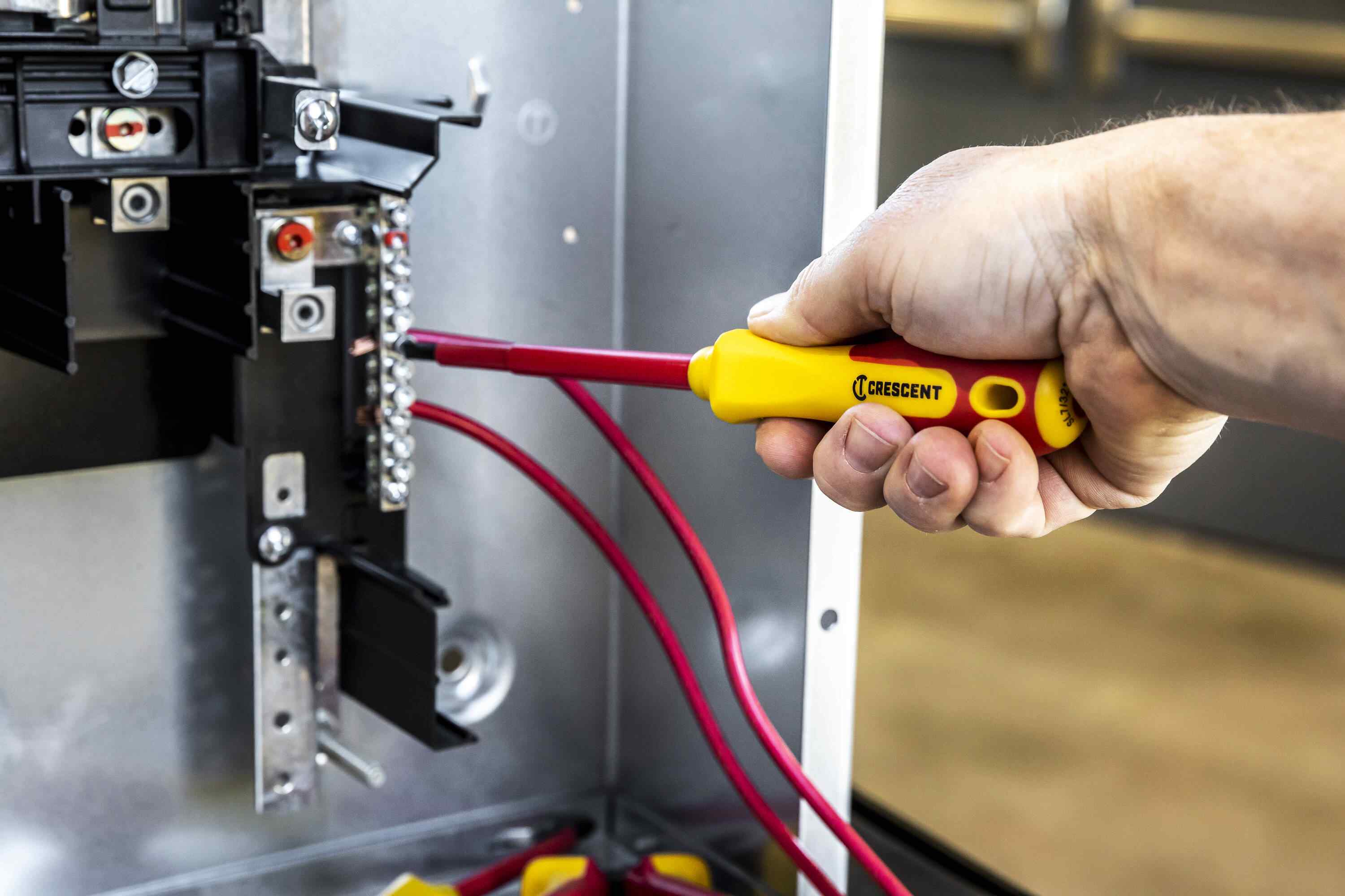 Electrician using a Crescent 1000V rated insulated slotted screwdriver to safely install wiring in a metal electrical panel.