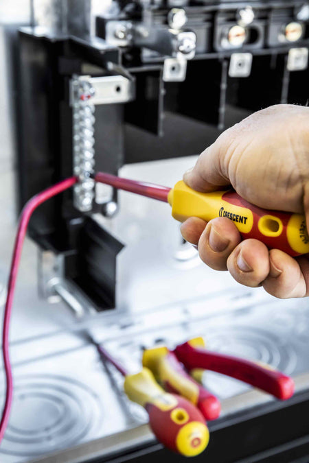 Close up of a professional using a Crescent VDE insulated Phillips screwdriver to tighten a terminal on an electrical circuit block.