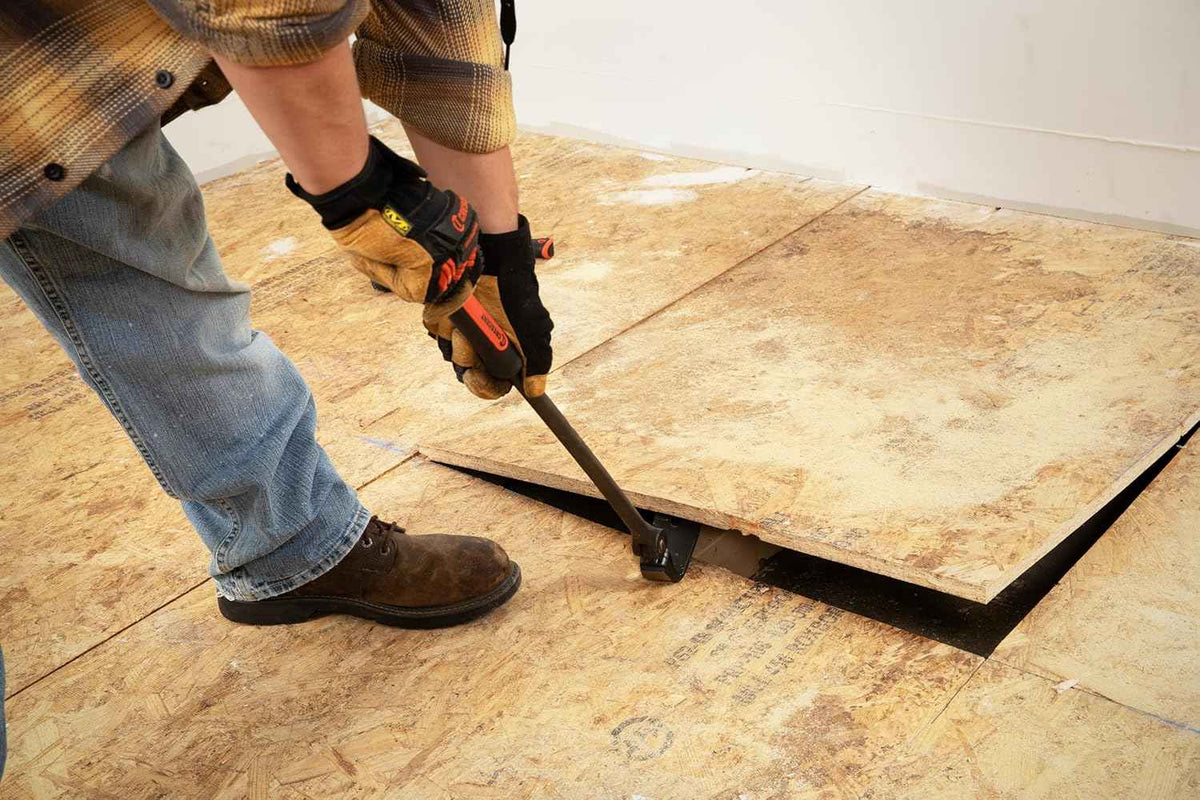 A worker using the Crescent 30-inch indexing flat pry bar to lift and remove a large section of OSB subflooring during a demolition project.