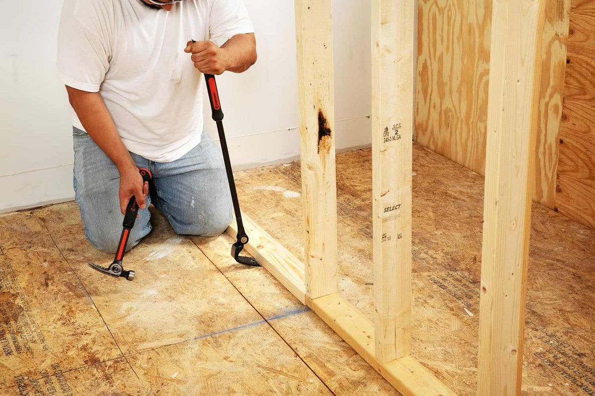 Construction professional using the adjustable head of the Crescent indexing pry bar to pry a bottom plate wall stud away from a wood floor.