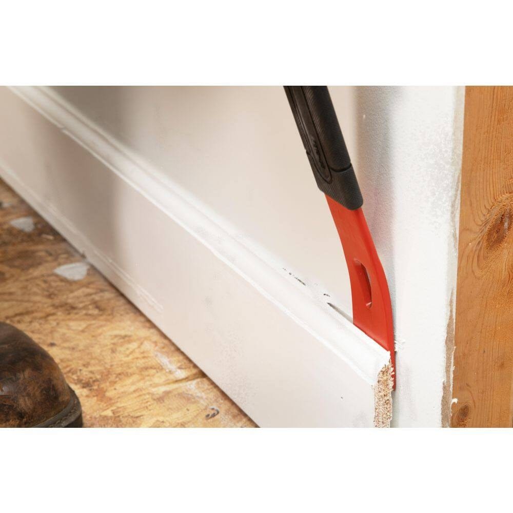 A close-up action shot of the Crescent flat pry bar being inserted behind a piece of white trim, showcasing how the precision ground edges allow for better access in narrow gaps to minimize damage to finished areas.