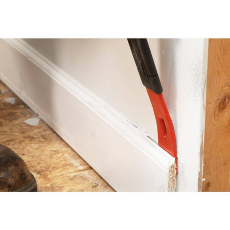A close-up action shot of the Crescent flat pry bar being inserted behind a piece of white trim, showcasing how the precision ground edges allow for better access in narrow gaps to minimize damage to finished areas.