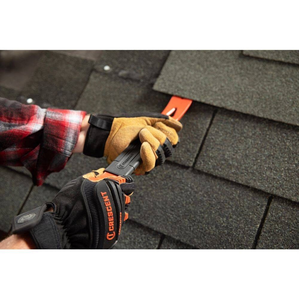 An action photograph of a worker wearing professional gloves using the Crescent flat pry bar to lift and remove asphalt roof shingles, highlighting the versatility of the beveled nail slots for different renovation tasks.