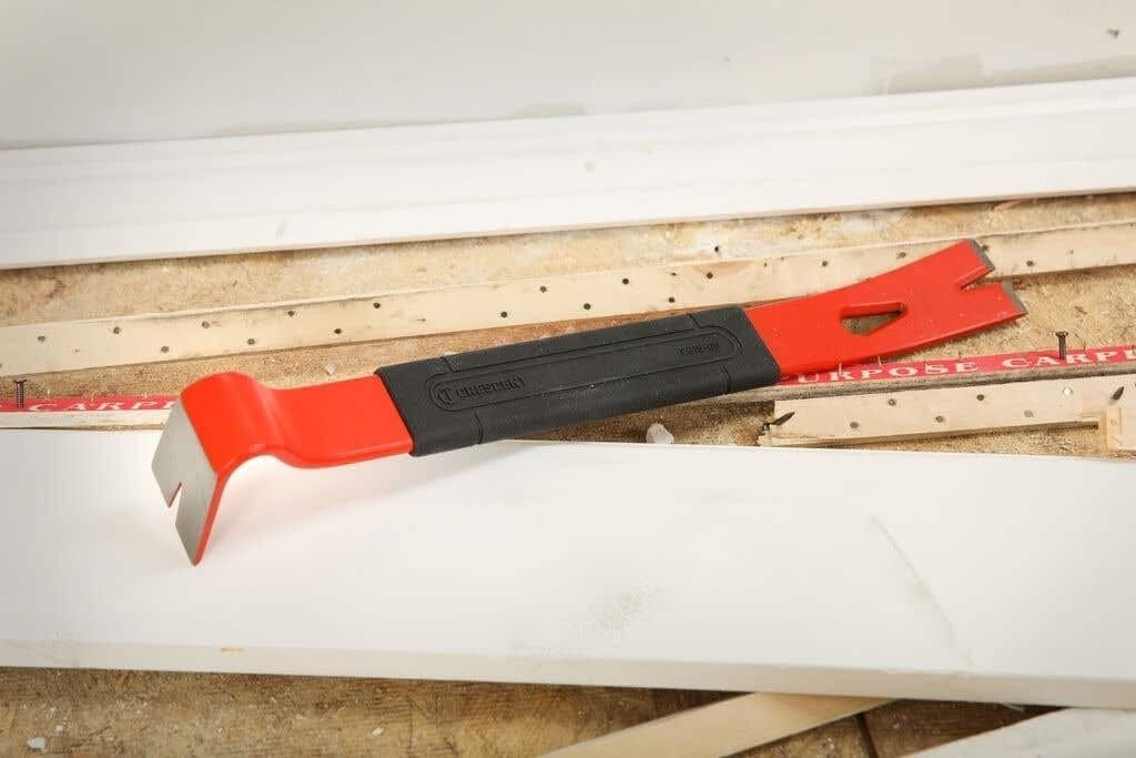 A lifestyle shot of the Crescent FB15-06 15-inch flat pry bar resting on a white trim board at a construction site, illustrating its portable size and readiness for professional wrecking and demolition work.