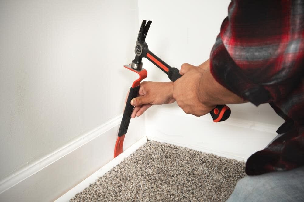 A person using the Crescent 7-inch flat pry bar to gently pull white decorative wall molding away from a wall, demonstrating the tool's precision ground edges for minimizing material damage.