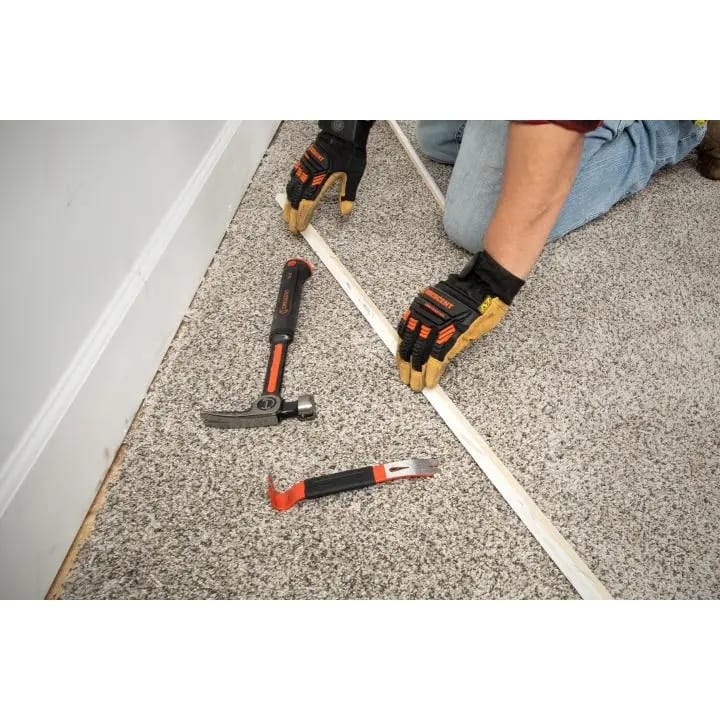 An overhead view of the Crescent 7-inch flat pry bar and a framing hammer resting on a carpeted floor next to a removed wooden trim piece.