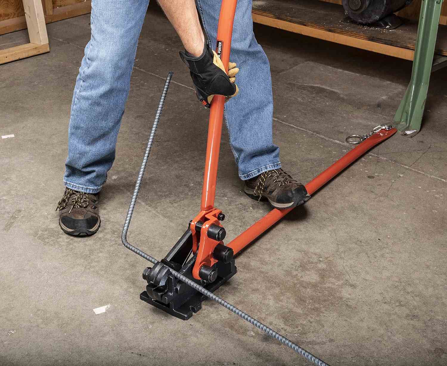 An action shot of a worker in jeans and boots using the floor-mounted H.K. Porter 0590RBJN to bend a long piece of rebar.