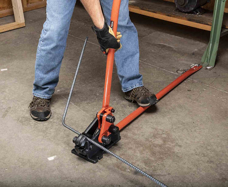 An action shot of a worker in jeans and boots using the floor-mounted H.K. Porter 0590RBJN to bend a long piece of rebar.