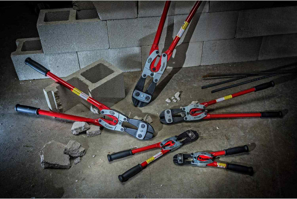 A group shot of various Crescent H.K. Porter PowerPivot bolt cutters in different sizes scattered on a jobsite floor with concrete blocks and rebar, showcasing the full professional product line for construction and industrial use.