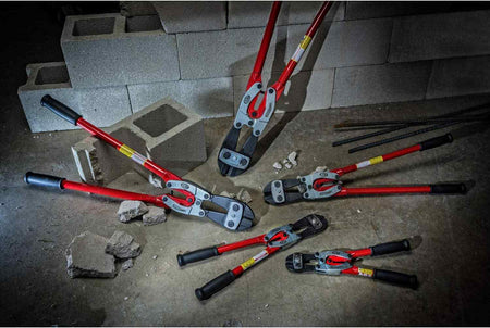 A group shot of various Crescent H.K. Porter PowerPivot bolt cutters in different sizes scattered on a jobsite floor with concrete blocks and rebar, showcasing the full professional product line for construction and industrial use.
