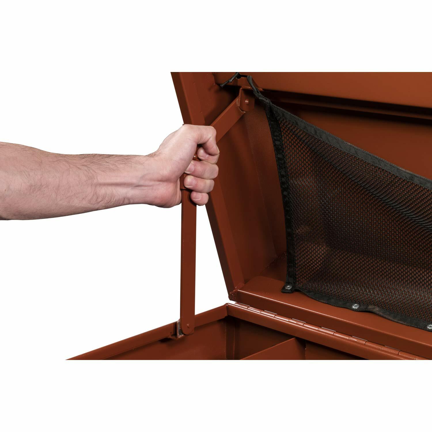 Person lifting the lid of a reddish-brown Crescent JOBOX chest, revealing a mesh pocket inside the lid and a metal support arm. Highlights lid organization and secure open-lid functionality for jobsite use.