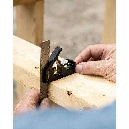 Lifestyle shot of a pair of hands using the combination square to mark a 90-degree cut line across a wooden 2x4 stud.