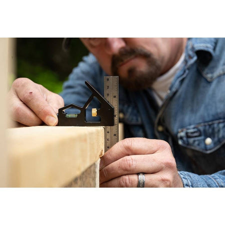Close-up action shot of a tradesman using the square to check the edge of a wooden beam, with the tool positioned to verify a right angle.