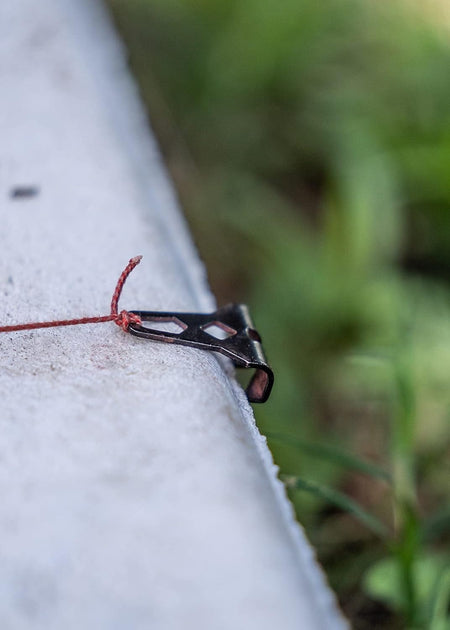Close-up of the Crescent Lufkin metal end hook secured to a concrete edge, showing the braided string under tension for a crisp layout snap.