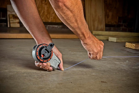 A person holds the Crescent Lufkin chalk reel and stretches the blue chalk line across a concrete floor to snap a straight line.