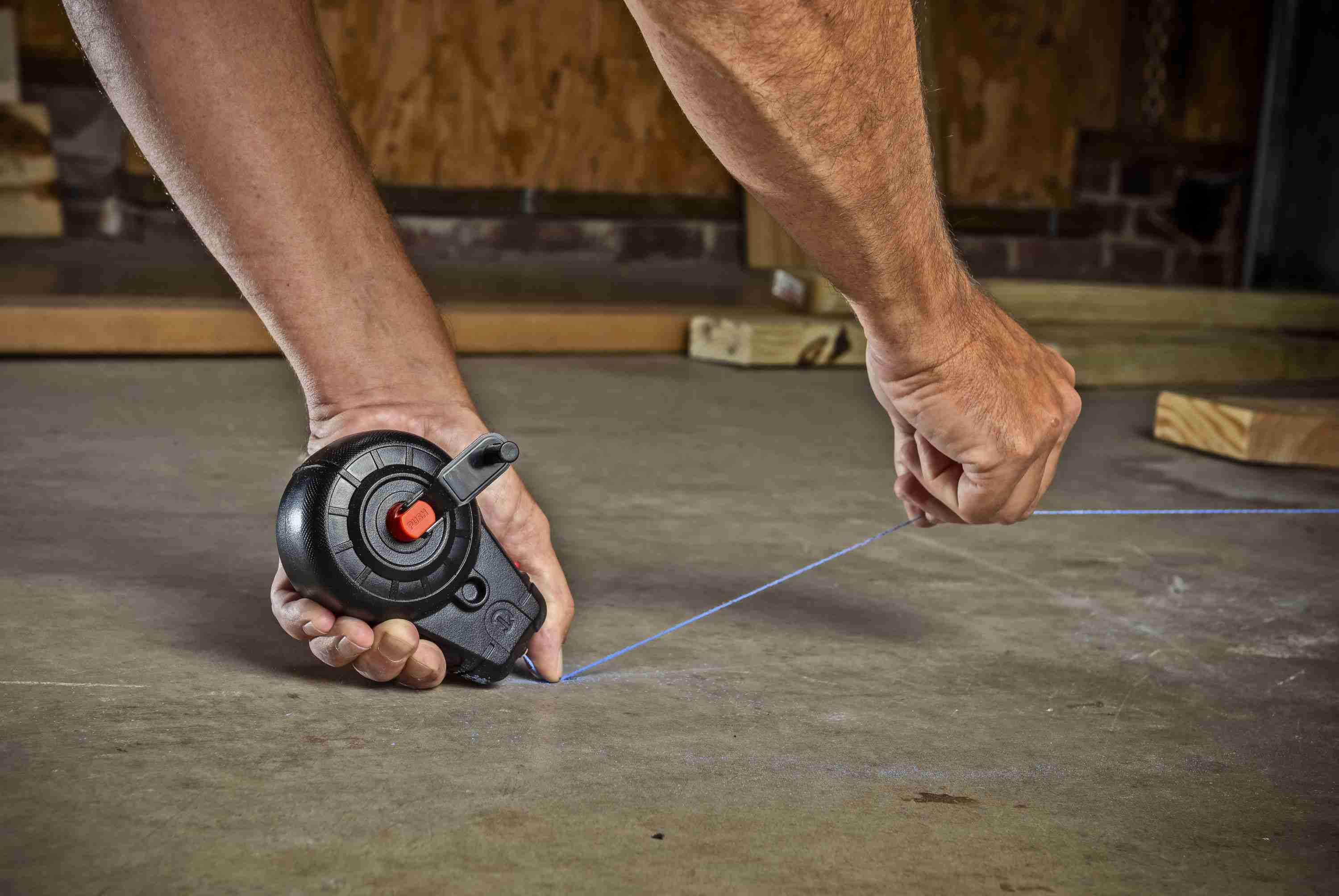 Action shot of a professional contractor using the Crescent Lufkin CLP100B chalk reel to snap a precise blue layout line on a concrete floor surface.