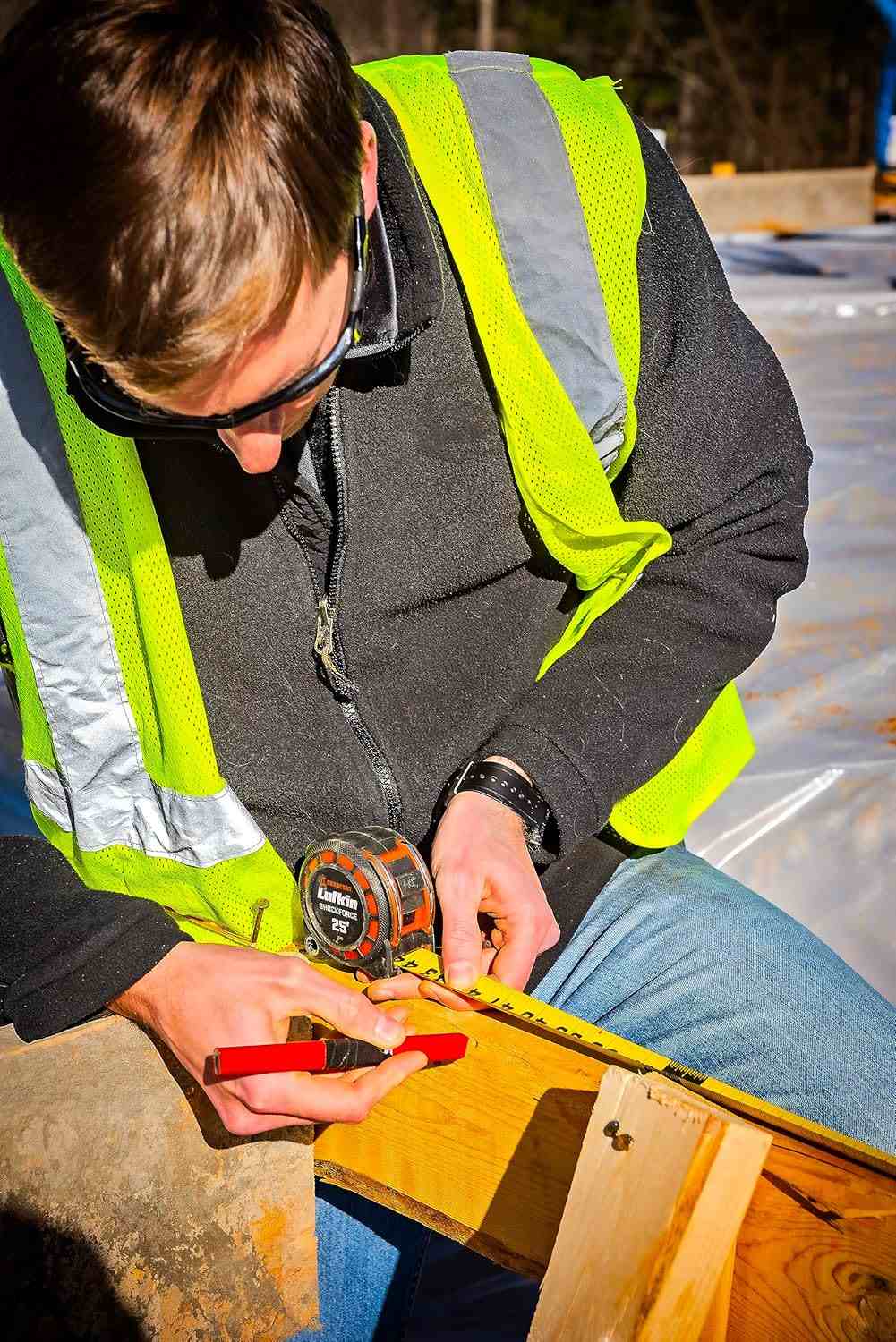 A detailed action shot of a professional woodworker using the Crescent Lufkin 25-foot tape measure to mark a precise measurement on a wooden board, highlighting the matte nylon-coated blade that reduces glare.
