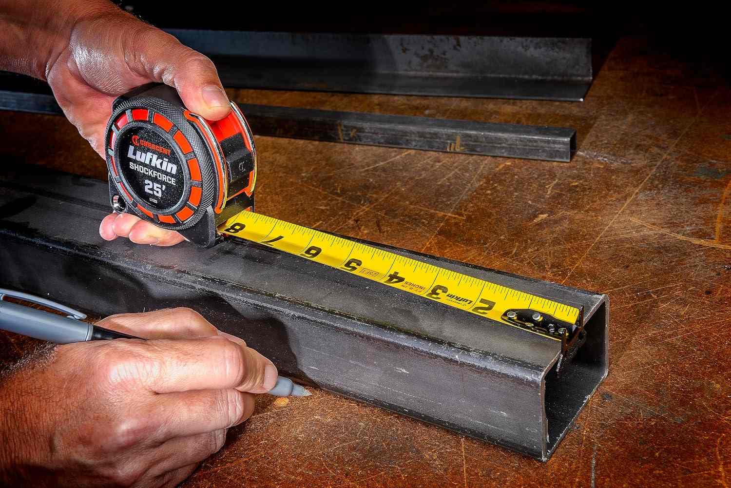An action photograph of a professional using the Crescent Lufkin Shockforce G1 tape measure to measure a steel beam, demonstrating the versatility of the 360-degree end hook for industrial layout tasks.