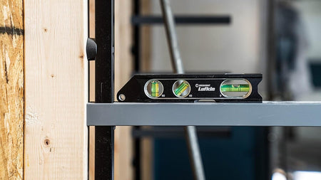 A lifestyle action shot showing the Crescent Lufkin torpedo level being used to verify the level of a horizontal steel beam in a commercial construction setting, highlighting the tool's industrial precision.