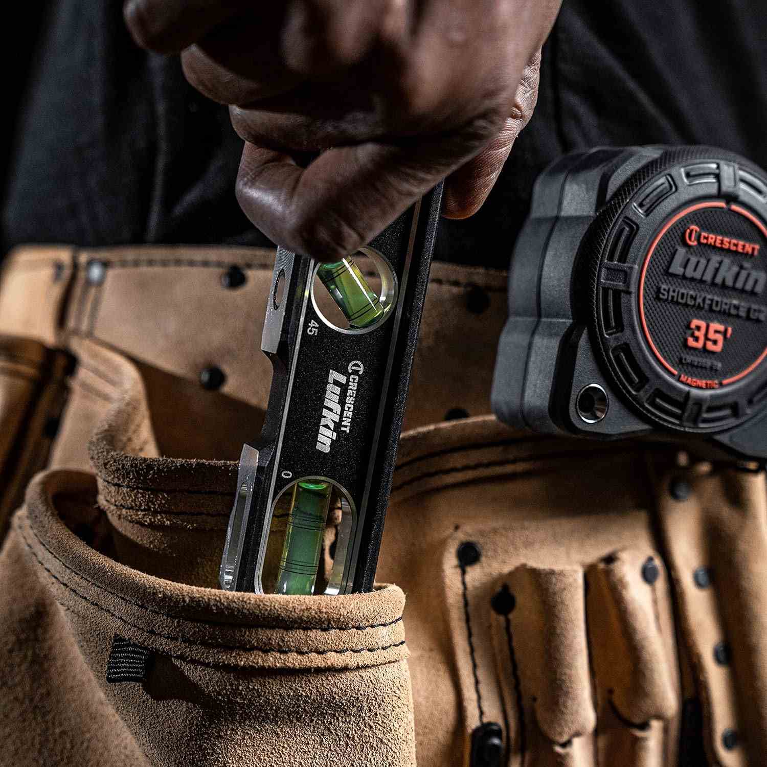 A lifestyle photograph showing a professional tradesman reaching into a suede tool pouch to retrieve the compact Crescent Lufkin aluminum billet level, demonstrating its portability and ease of access on the job.