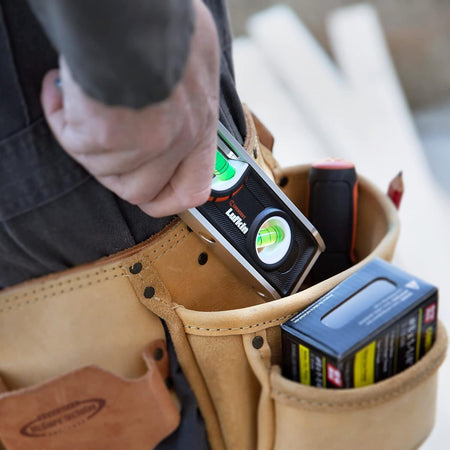 A lifestyle photograph showing a professional tradesman reaching into a tan leather tool pouch to retrieve the compact Crescent Lufkin aluminum torpedo level, demonstrating its portability and ease of access on the job.