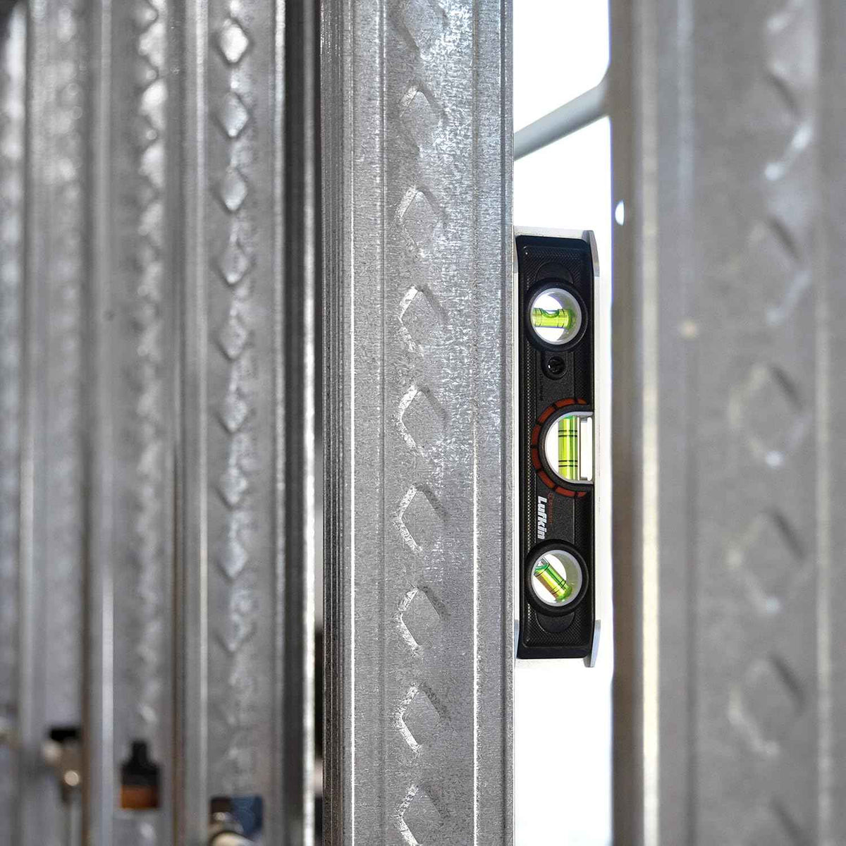 An action photograph of the Crescent Lufkin LTLA1100-02 torpedo level magnetically attached to a vertical steel wall stud, demonstrating the strong holding power of the rare earth magnets on a construction site.