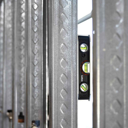 An action photograph of the Crescent Lufkin LTLA1100-02 torpedo level magnetically attached to a vertical steel wall stud, demonstrating the strong holding power of the rare earth magnets on a construction site.