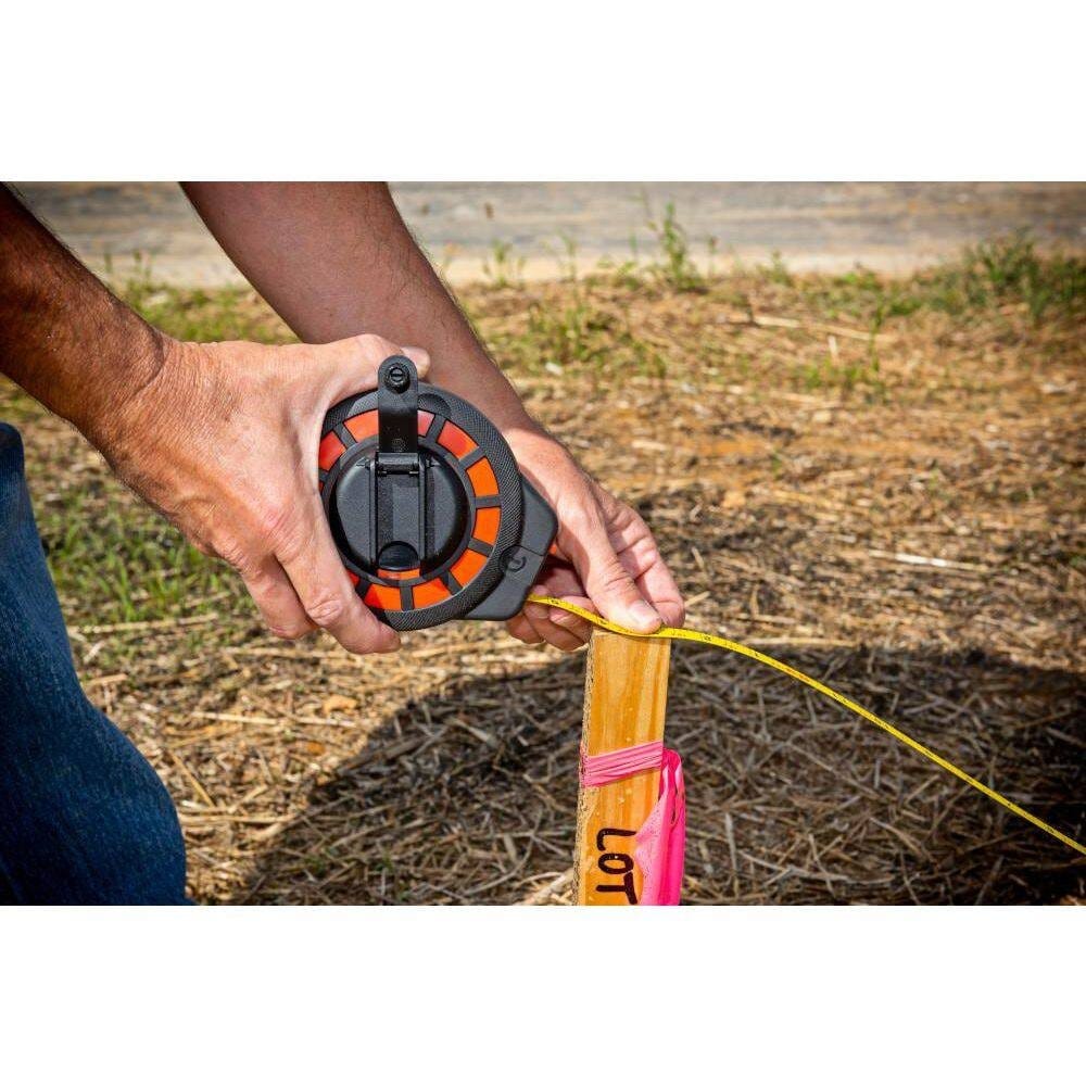 A professional surveyor utilizing the Crescent Lufkin ST100-07 100-foot long tape to measure from a wooden site stake, demonstrating the precision of the high-contrast yellow steel blade.